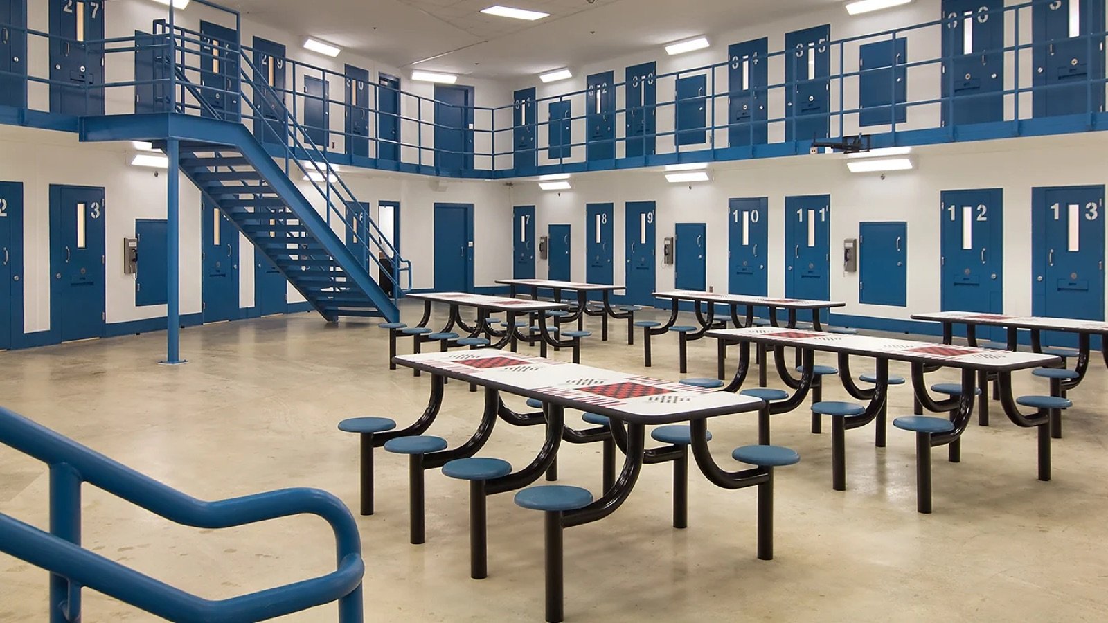 A housing pod at Rappahannock Regional Jail: a two-tier block of cell doors around an open floor with fixed steel tables.